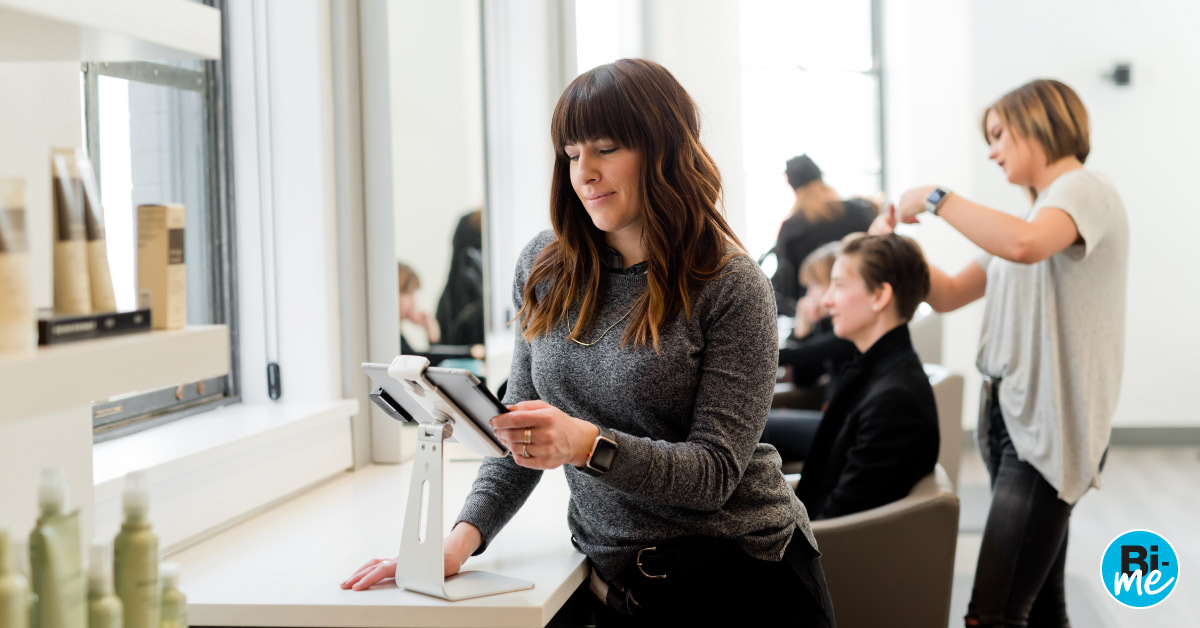 A lady busy on a tablet with people getting their hair cut in a hair salon